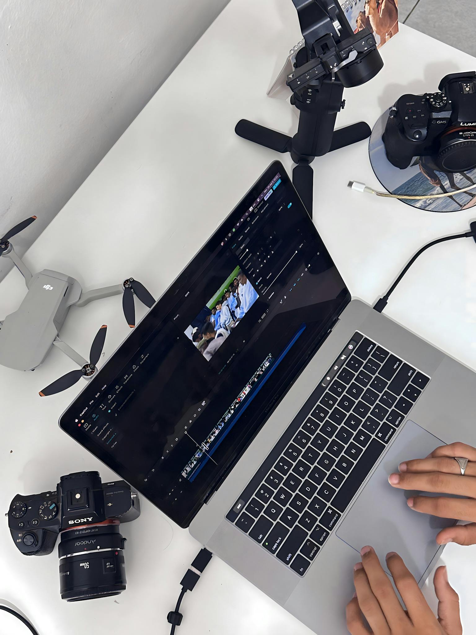 Hands editing aerial footage on laptop with camera, drone, and stabilizer.